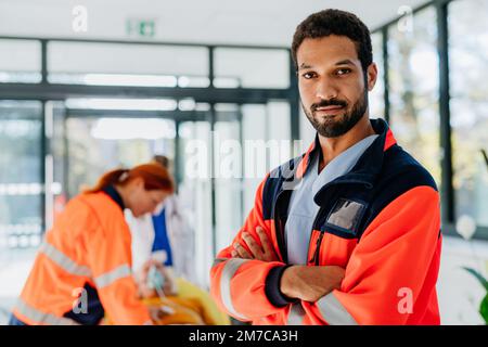 Ritratto dell'uomo soccorritore, i suoi colleghi si prendono cura del paziente da un'ambulanza. Foto Stock