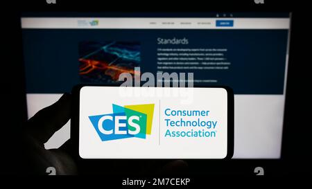 Persona che tiene lo smartphone con il logo della US Consumer Technology Association (CTA, CES) sullo schermo davanti al sito Web. Messa a fuoco sul display del telefono. Foto Stock