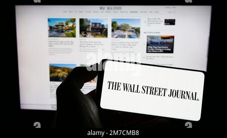 Persona che tiene il cellulare con il logo del giornale degli Stati Uniti il Wall Street Journal sullo schermo di fronte alla pagina web. Messa a fuoco sul display del telefono. Foto Stock