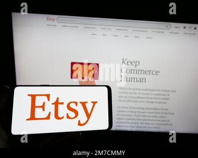 Persona che tiene in mano uno smartphone con il logo della società di e-commerce statunitense Etsy Inc. Sullo schermo di fronte al sito Web. Messa a fuoco sul display del telefono. Foto Stock