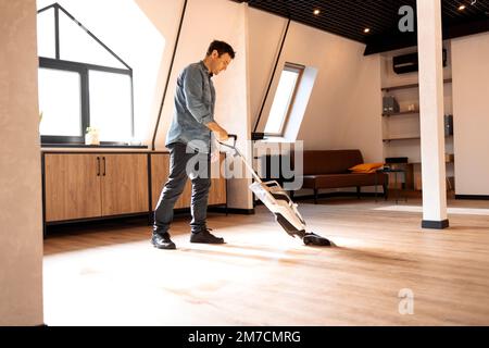 Brunette uomo che aspira pavimenti in legno in soppalco con aspirapolvere Foto Stock