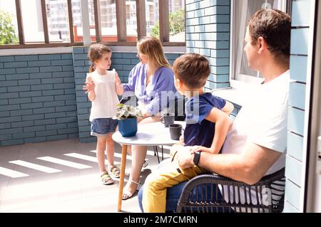 La famiglia ha fatto un buon caffè nel patio sul tetto di casa la mattina. Padre, madre, così e figlia che parlano insieme. Famiglia cura e divertimento Foto Stock