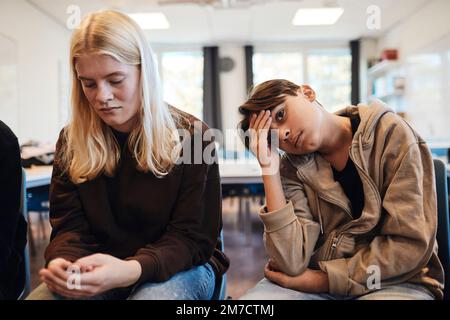 Triste adolescente seduto da ragazza bionda in classe durante la terapia Foto Stock