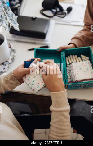 Le mani di una studentessa che tiene imbottiture sanitarie e tamponi al tavolo in ufficio scolastico Foto Stock