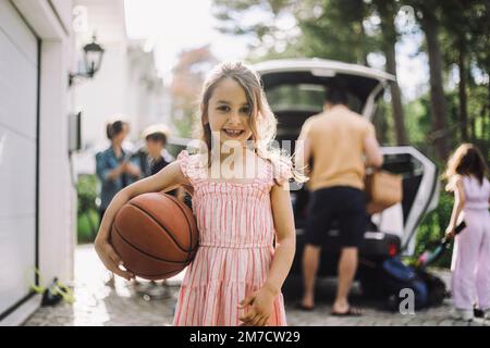 Ritratto di una ragazza sorridente che tiene il basket con la famiglia sullo sfondo Foto Stock