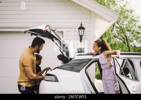 Ragazza sorridente che parla con il padre che carica roba nel tronco dell'automobile Foto Stock