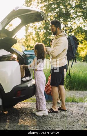 Vista laterale di figlia e padre che scaricano i bagagli dal bagagliaio dell'auto Foto Stock