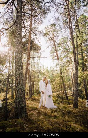 Bouquet medio adulto che tiene la sposa guardando lo sposo in piedi tra gli alberi nella foresta Foto Stock