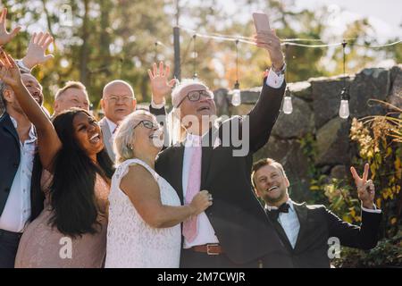 Felice coppia anziana in giovane età che prende selfie con la famiglia e gli amici attraverso lo smartphone Foto Stock