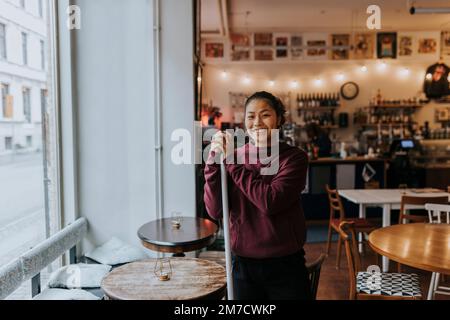 Ritratto di felice padrona di casa in piedi al tavolo in caffetteria Foto Stock