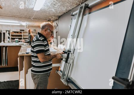Vista laterale dell'artigiano che utilizza la serigrafia mentre lavora in officina Foto Stock