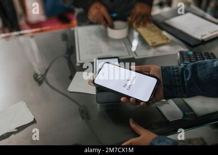 Mano di donna che effettua il pagamento contactless attraverso lo smartphone in officina Foto Stock