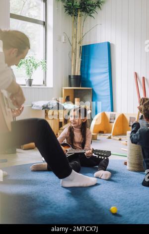 Ragazza che impara la chitarra da un assistente maschio di cura del bambino all'asilo Foto Stock