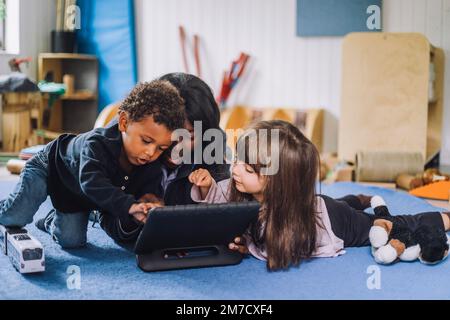 Insegnante che condivide il tablet digitale con i bambini nel centro di assistenza bambini Foto Stock