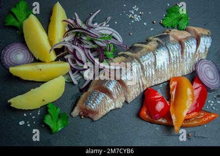 Filetto di aringa marinato a fette con cipolle, patate, aneto e pepe. Sfondo nero. Vista dall'alto. Filetto di aringa salata con patate. Foto Stock