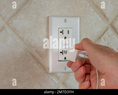 Collegamento del cavo usb elettrico e collegamento del caricabatterie alla presa a muro. Adattatore di alimentazione per telefono cellulare e cavo nella presa a muro GFCI. Foto Stock