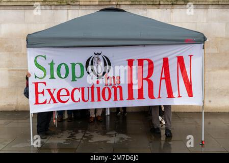 Stop esecuzione in Iran banner di protesta. Manifestanti che si riparano dalla pioggia prima di un raduno di protesta a Londra, Regno Unito Foto Stock
