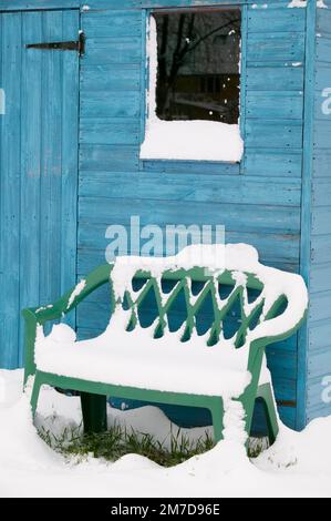 Un capannone blu brillante e una panca di plastica coperta di neve dopo una tempesta invernale su un'assegnazione nel Regno Unito. Foto Stock