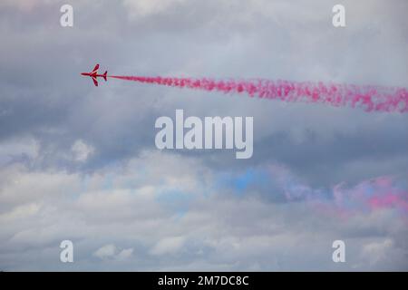 Un aereo della famosa squadra di esposizione Red Arrows si sfoca davanti al fumo rosa in arrivo mentre partecipa a uno spettacolo. Foto Stock