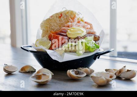 Piatto con hamburger con salmone e gamberi su tavolo decorato con conchiglie, isole Lofoten, Norvegia Foto Stock