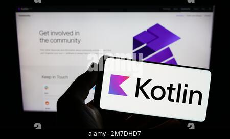 Persona che tiene lo smartphone con il logo del linguaggio di programmazione Kotlin sullo schermo di fronte al sito Web. Messa a fuoco sul display del telefono. Foto Stock