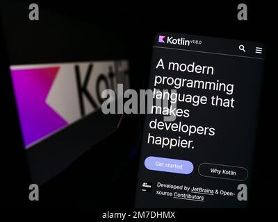 Persona che tiene in mano smartphone con sito web di lingua di programmazione Kotlin sullo schermo di fronte al logo. Messa a fuoco al centro del display del telefono. Foto Stock