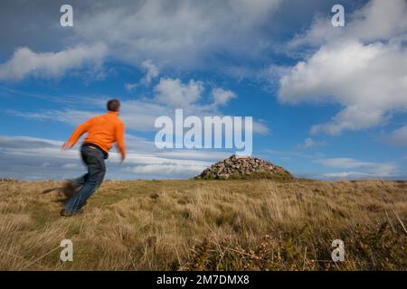 Un camminatore corre gli ultimi metri ad un tumulo di pietra sulla cima della collina di Bossington dove gli escursionisti collocano una pietra portata dal basso verso l'alto che si affaccia sulla baia di Porlock, somerset. Foto Stock