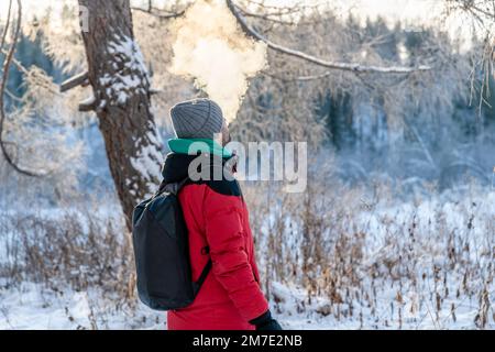 un uomo d'inverno al freddo esala una nuvola di vapore, fumo all'aperto Foto Stock