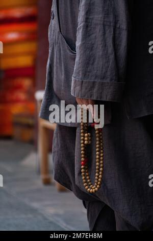 Uno scatto verticale di un monaco con vestiti grigi che reggono un rosario Foto Stock