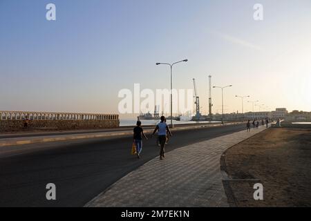 Persone che camminano per lavorare lungo la strada sopraelevata all'alba a Massawa Foto Stock