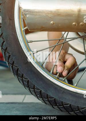 Mani di un uomo controllare la pressione del generatore di gas e gonfiare uno pneumatico su una motocicletta con un compressore pneumatico. Man controllo della pressione dell'aria e riempimento della pressione dei pneumatici Foto Stock