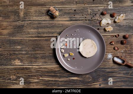 Un piatto con foie gras francese servito con noci, pepe, sale e frutta secca sul tavolo di legno, vista dall'alto con spazio copia Foto Stock