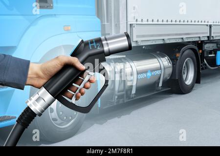 Mano con ugello di rifornimento H2 sullo sfondo di un semi-camion a celle a combustibile idrogeno con serbatoio del gas a bordo. Concetto di veicolo commerciale ecocompatibile Foto Stock