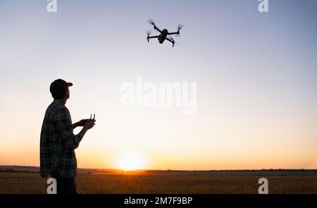 Farmer controlla l'irroratrice di droni con un tablet al tramonto. Agricoltura intelligente e agricoltura di precisione Foto Stock