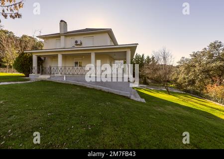 Casa singola residenziale indipendente su un terreno in pendenza con erba e alberi Foto Stock