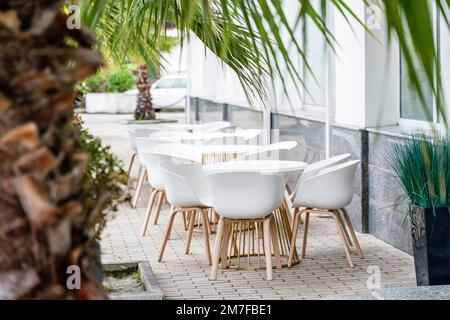 Street cafè con sedie bianche, verde fogliame intorno. Senza persone, turismo, viaggi. Foto Stock