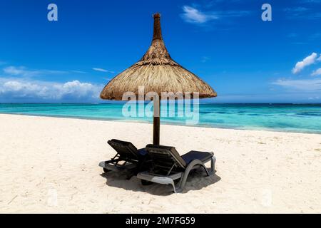 Spiaggia di sabbia bianca e soleggiata con ombrellone di paglia e sedie a sdraio e mare tropicale in un resort tropicale Foto Stock