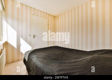 un letto in una camera con tappezzeria a righe sulle pareti e una porta aperta che conduce ad un'altra stanza Foto Stock