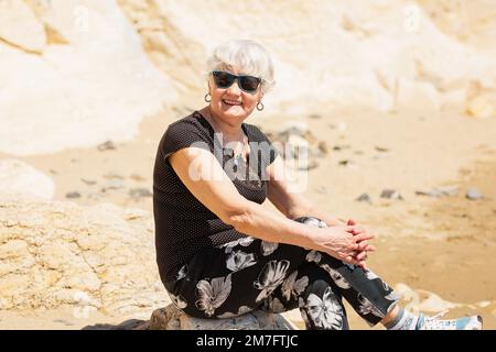 Donna anziana in abiti neri seduti su una roccia vicino al mare Foto Stock