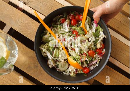 Donna che tiene in mano una ciotola con deliziosa insalata vegetariana sana di verdure su un tavolo di legno. Foto Stock