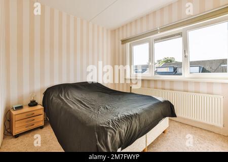 una camera da letto con carta da parati a righe sulle pareti e un letto nero sparso sulla testata della camera Foto Stock