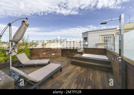 Terrazza in casa attico tutto coperto in legno di acacia tavole con una vasca idromassaggio, doccia in acciaio inossidabile e amache in rattan e vista sulla città Foto Stock