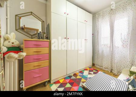 Camera per bambini con cassettiera con ruote e cassetti colorati e armadio a quattro sezioni in legno bianco Foto Stock