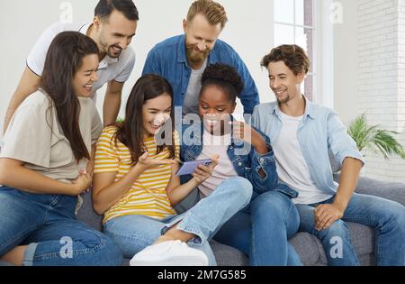 Gruppo di persone a casa che guardano foto e video divertenti insieme sul telefono cellulare. Foto Stock