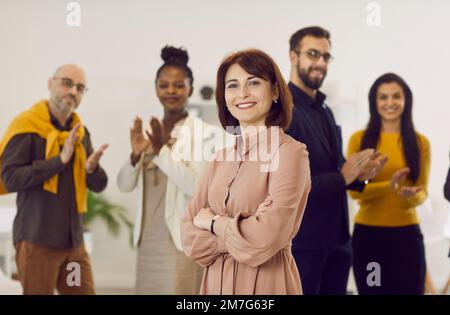 Ritratto di una donna leader di successo con un team di dipendenti applaudente in background Foto Stock