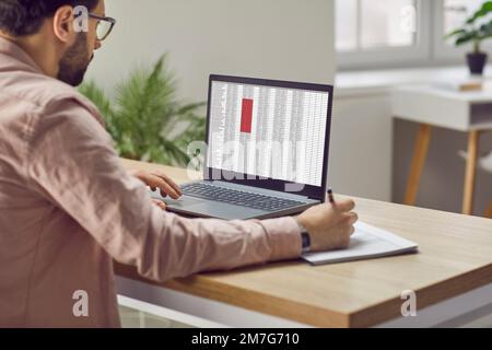 Financier maschile concentrato utilizzando un computer portatile che lavora in ufficio con i dati inseriti in un foglio di calcolo. Foto Stock