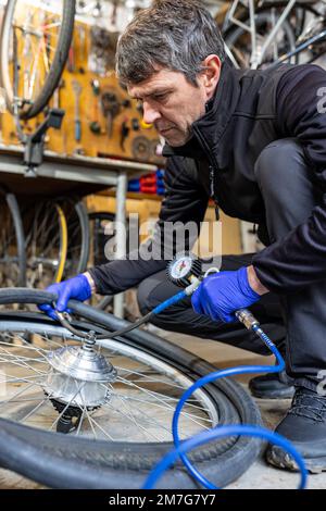 Tecnico ciclistico manutenzione bici, soffiatura pneumatici con pompa a pressione manuale in officina Foto Stock