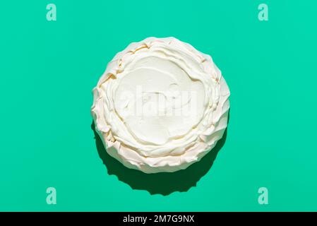 Vista sopra con una torta Pavlova fatta in casa, minimalista su un tavolo verde. Dessert tradizionale australiano, crosta croccante di meringa riempita con panna montata Foto Stock