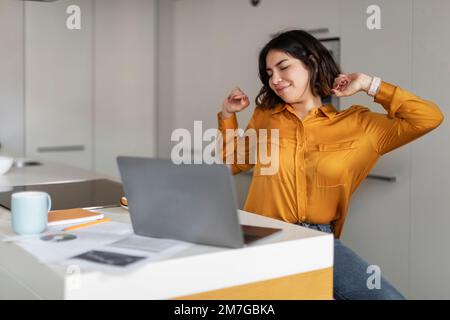 Giovane donna araba sorridente che si allunga dopo una giornata di lavoro in ufficio a casa Foto Stock