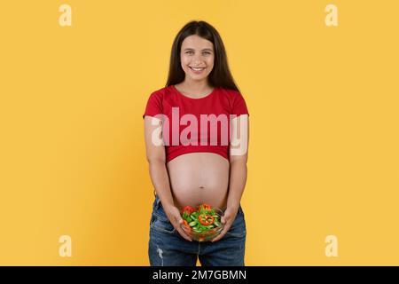 Bella giovane donna incinta con ciotola di insalata di verdure fresche in mano Foto Stock